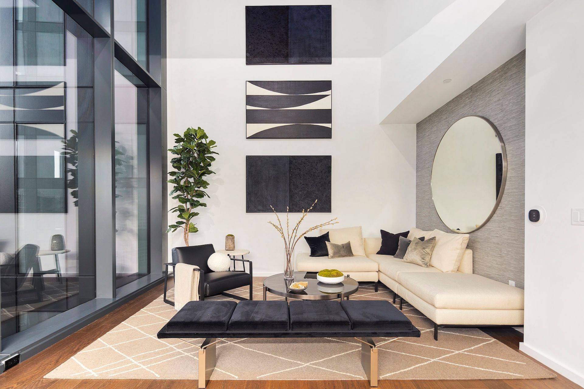 Modern living room with cream sectional, black coffee table, wall art, and large glass windows.