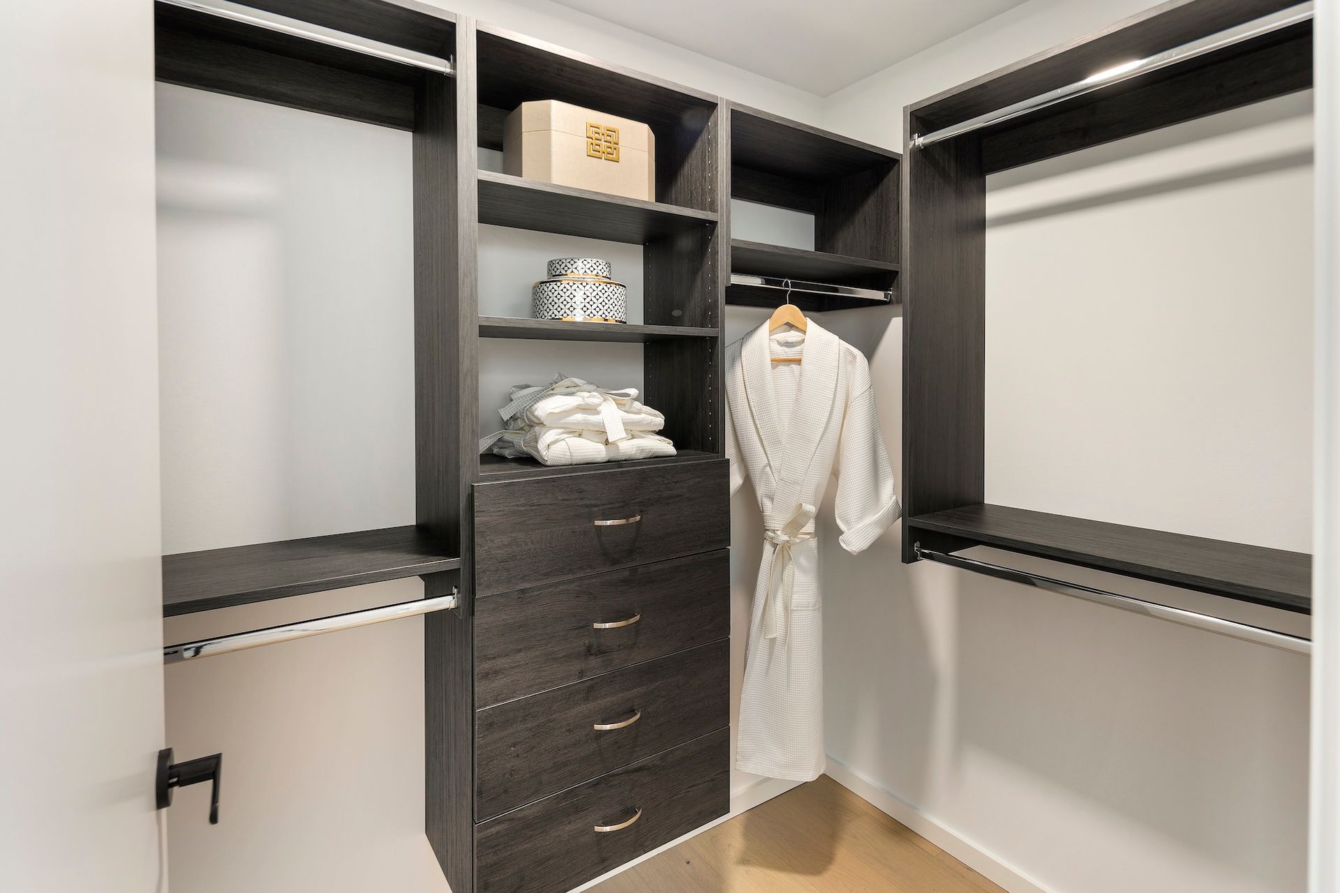 Walk-in closet with open shelving, drawers, hanging rods, and white robe hanging inside.