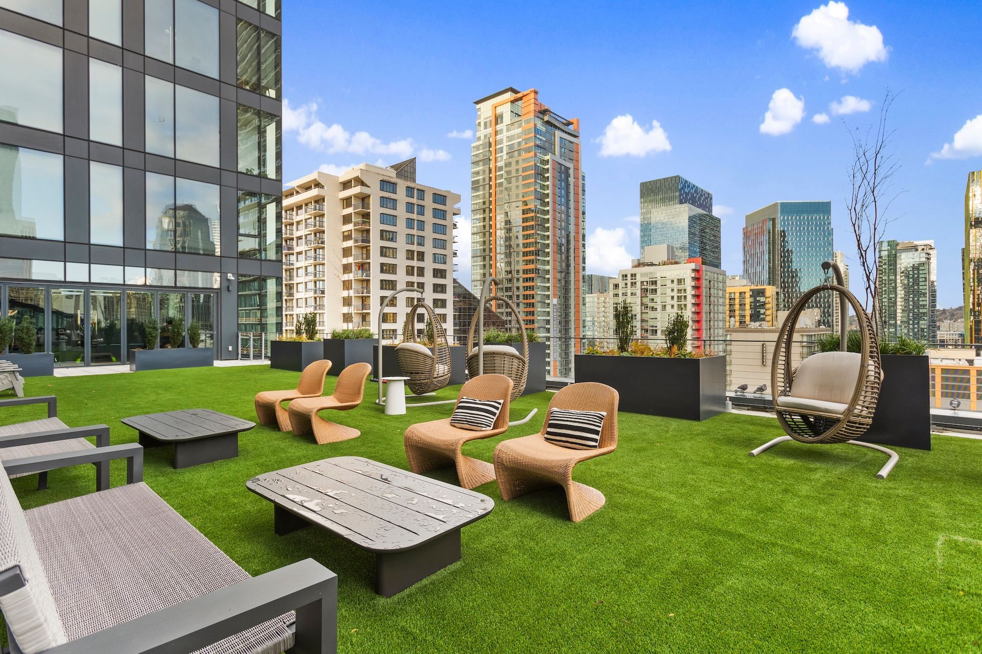 Rooftop terrace with lounge chairs, green turf, and city skyline under a blue sky.