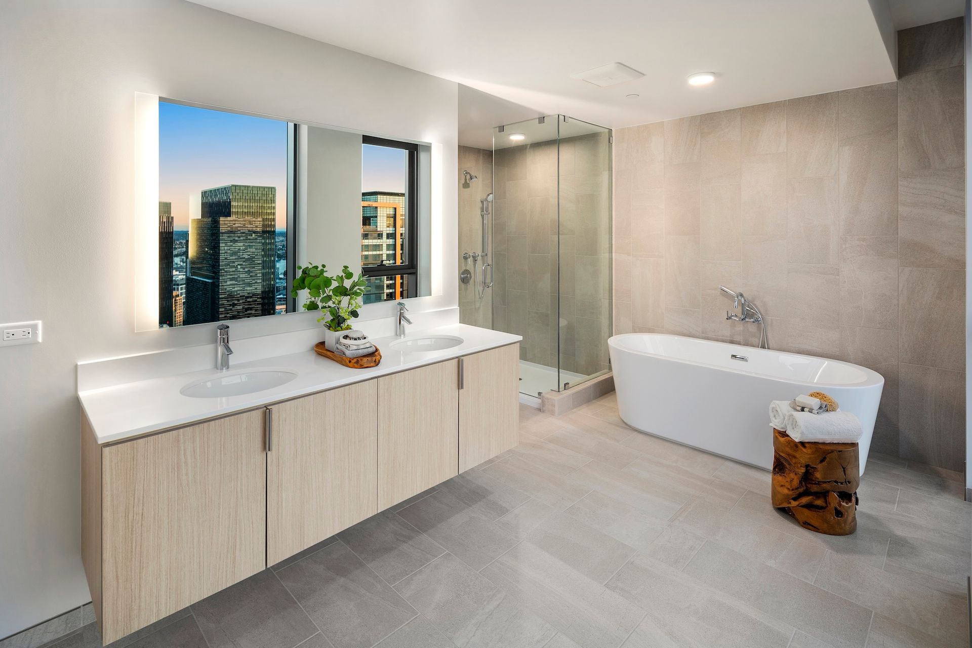 Modern bathroom with double vanity, freestanding tub, gray tile, and city-view window.