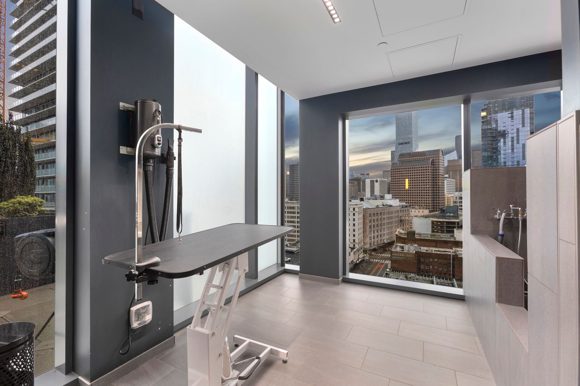 Modern exam room with exam table, medical equipment, and large window overlooking city buildings.