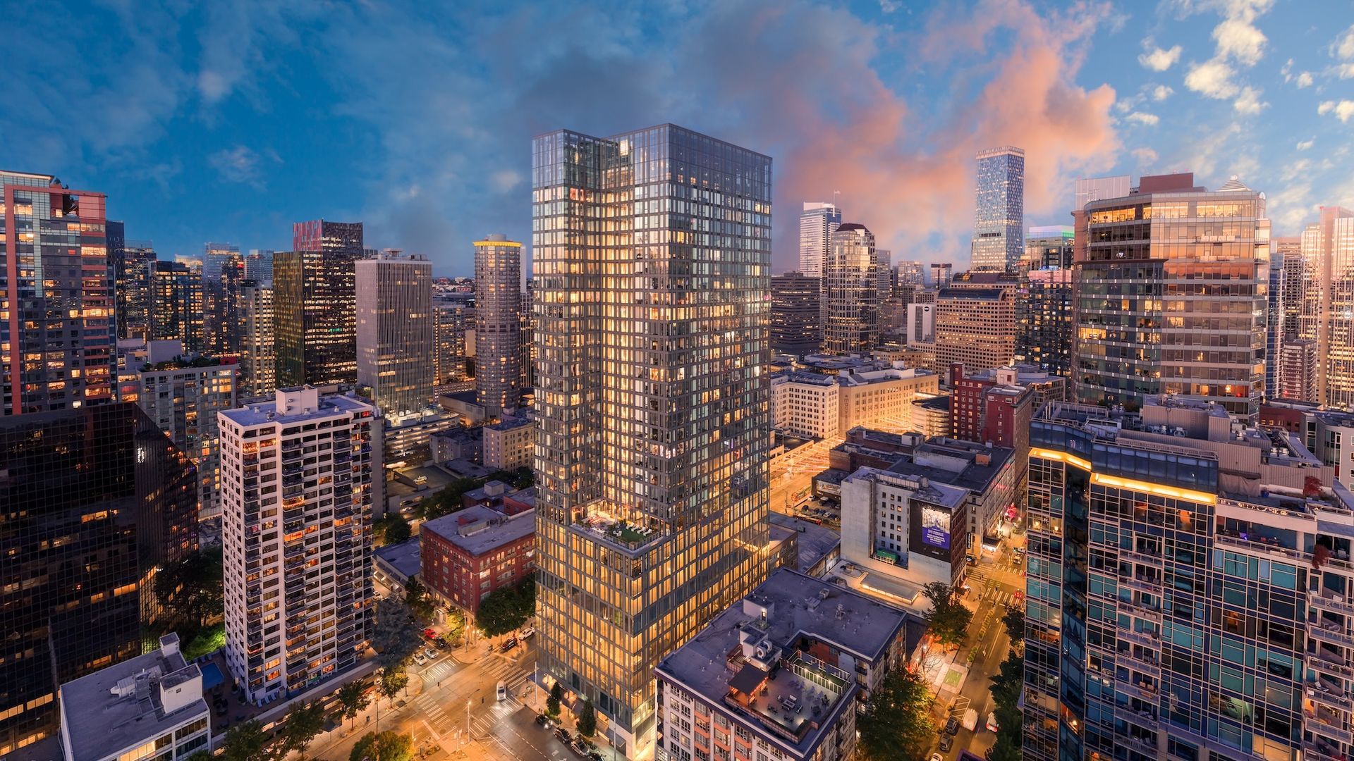 City skyline at dusk with lit high-rise buildings and a central glass tower under a blue-pink sky