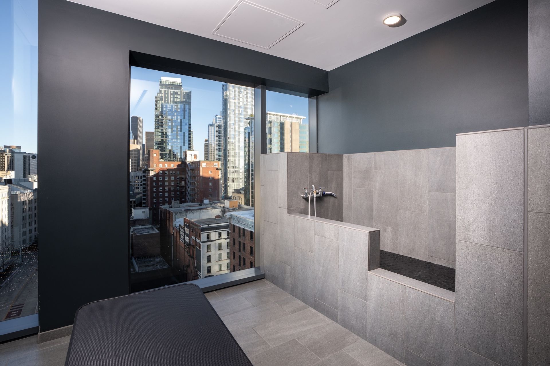 Modern restroom with gray stalls and a large window overlooking a city skyline.