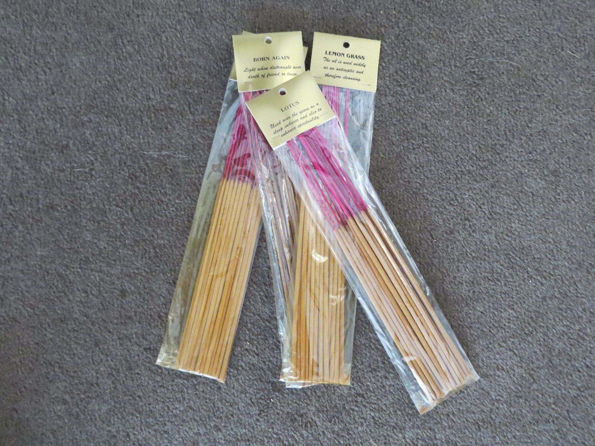 Three plastic-wrapped bundles of pink incense sticks with beige bamboo bases, arranged on a grey carpet.