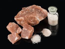 Chunks of pink Himalayan salt, along with a vial and two piles of salt crystals, arranged against a black backdrop.