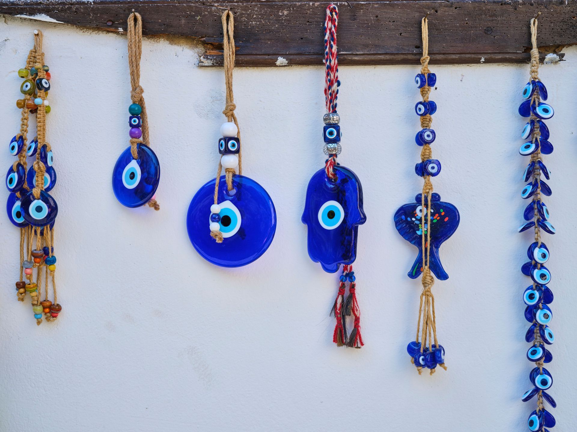 Blue evil eye and beaded wall hangings on a white wall with a wooden beam.