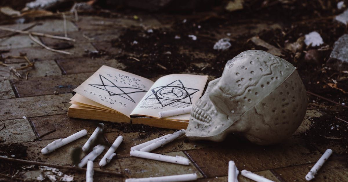 A skull, an open book with occult symbols, and scattered white chalk on a dark, dirt-covered stone ground.