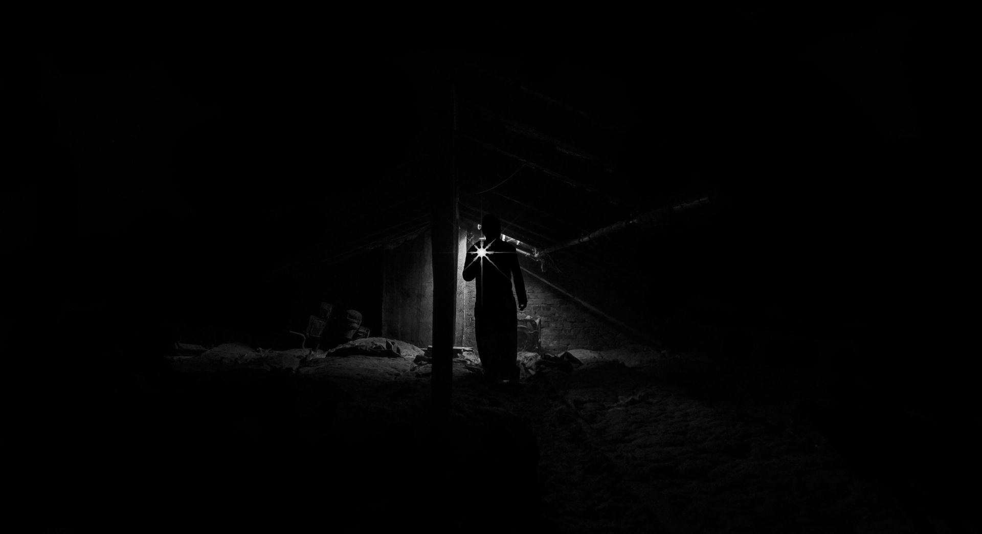 Dark black-and-white scene of a lone figure standing under a streetlight in a snowy landscape.