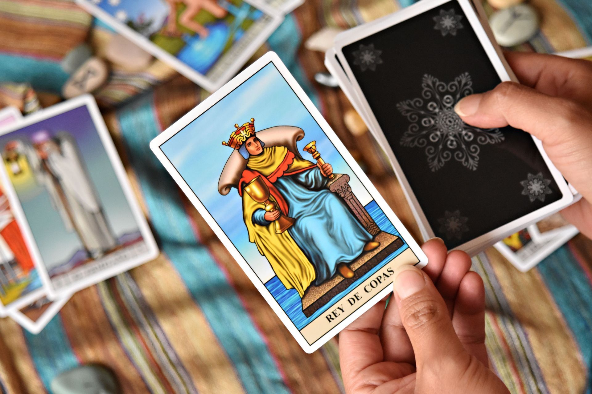 Hands holding tarot cards over a spread of colorful cards on a wooden table