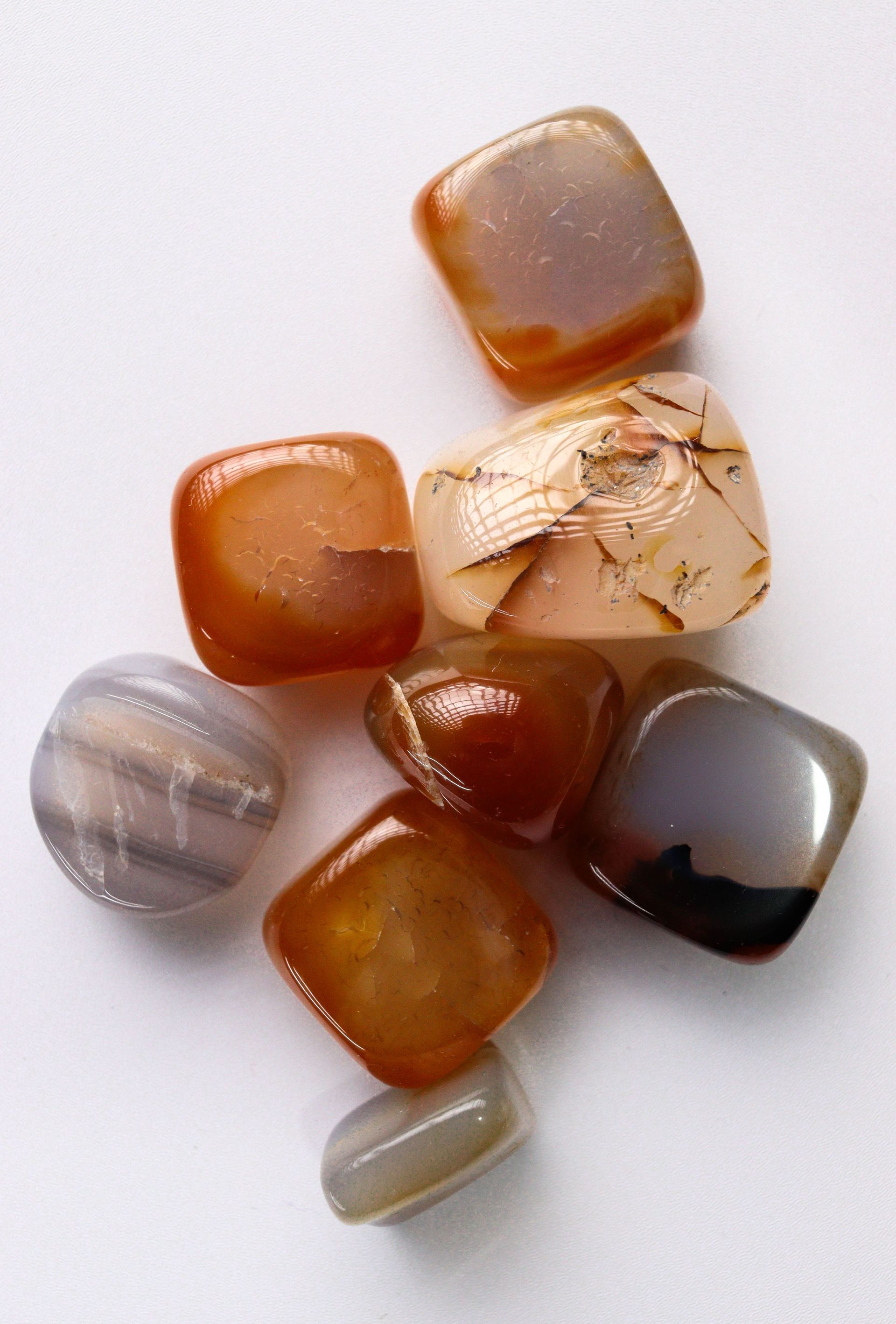 Assorted polished gemstone beads in amber, gray, cream, and black on a white background Carnelian