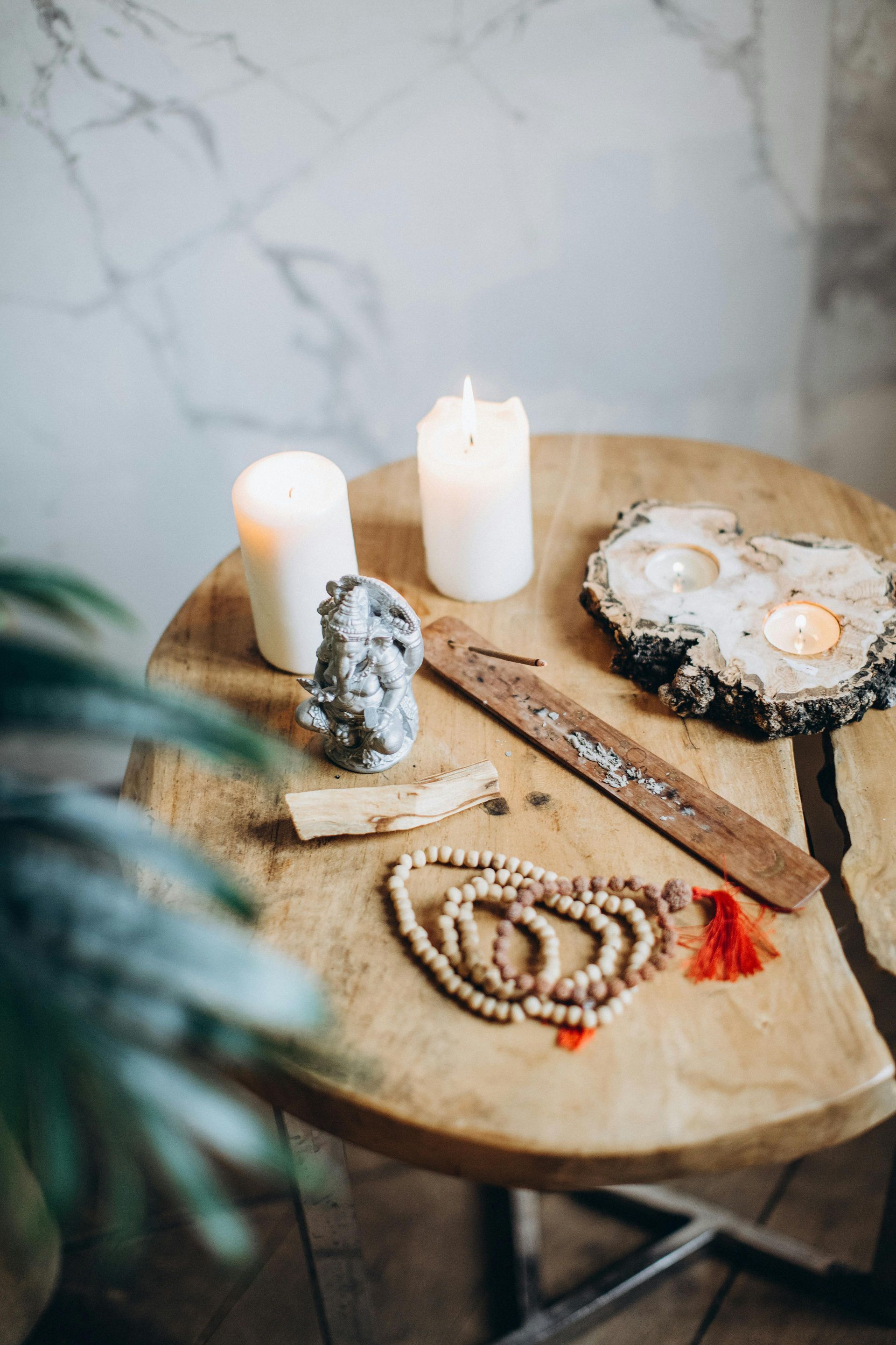 A wooden table displays lit candles, beads, crystals, and incense, suggesting a spiritual or meditation setting.