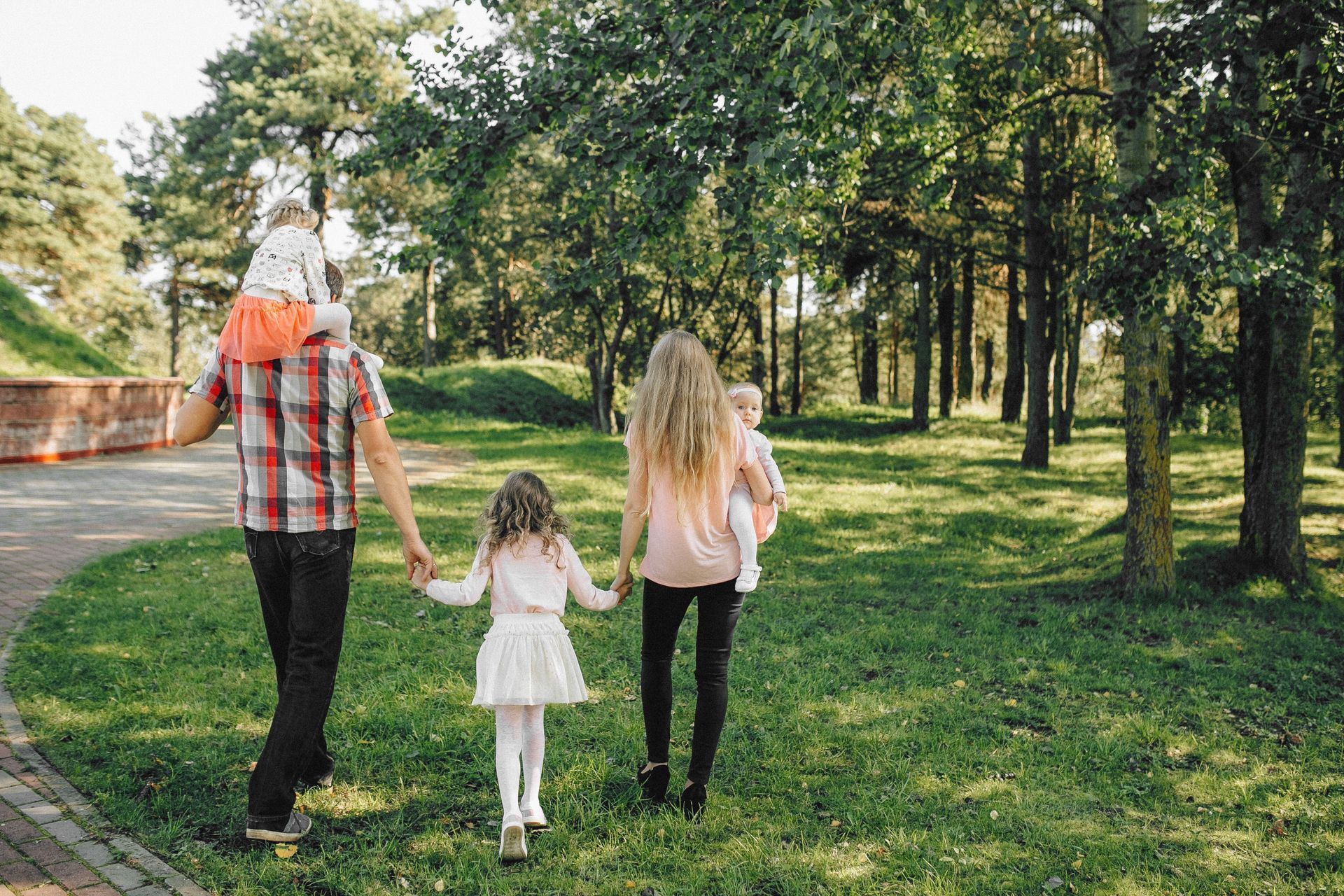 Three people walking hand in hand through a sunny park with trees and grass.