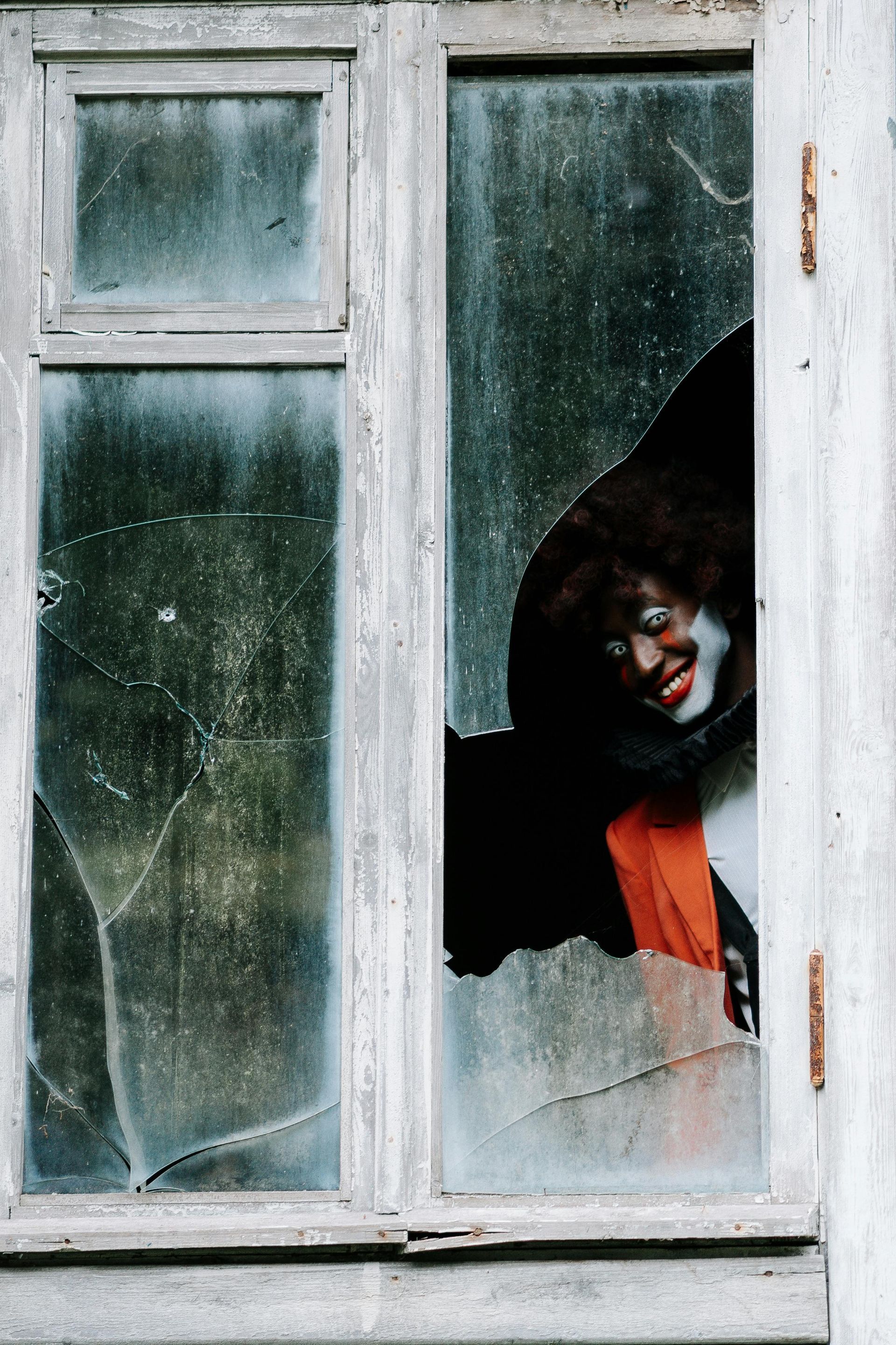 A clown is peeking out of a broken window