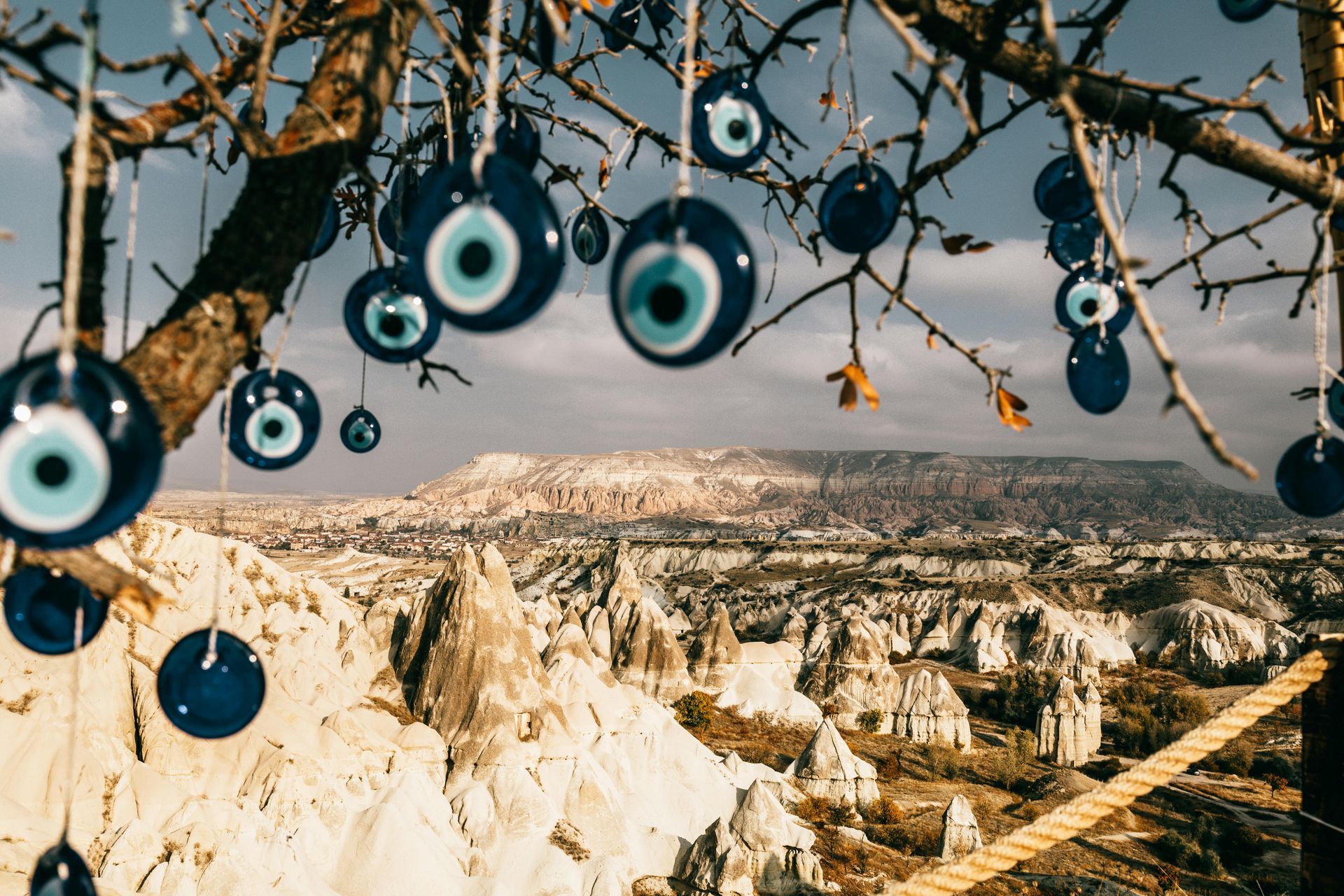 Blue evil eye charms hang from a tree, overlooking a scenic canyon landscape.