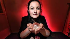 Sarah Kulkens is holding a crystal ball in her Belgrave shop with Tarot Cards and crystals on the table,