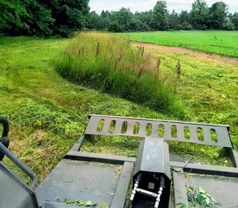 Farm machinery overlooking a grassy field and tree line under overcast sky