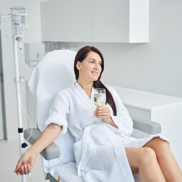 a woman in a bathrobe is sitting in a hospital chair holding a glass of wine .