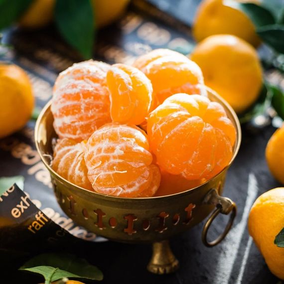 A bowl of tangerines is surrounded by tangerines on a table.