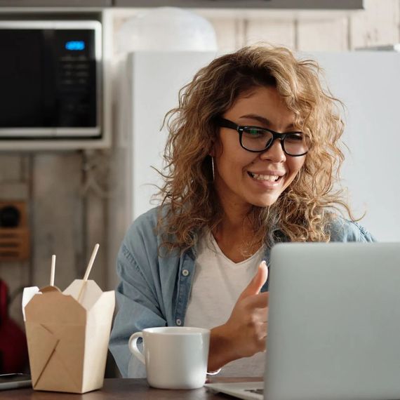 A woman is sitting at a table with a laptop and a cup of coffee.