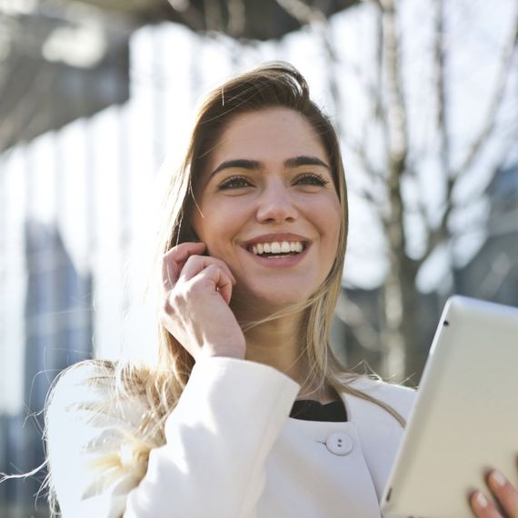 a woman is smiling while talking on a cell phone and holding a tablet