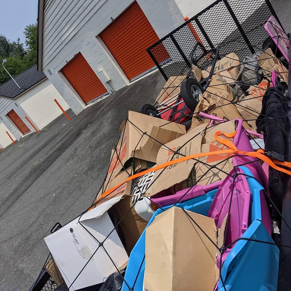 A utility trailer packed with cardboard boxes and colorful plastic bins, parked outside a row of self-storage units.