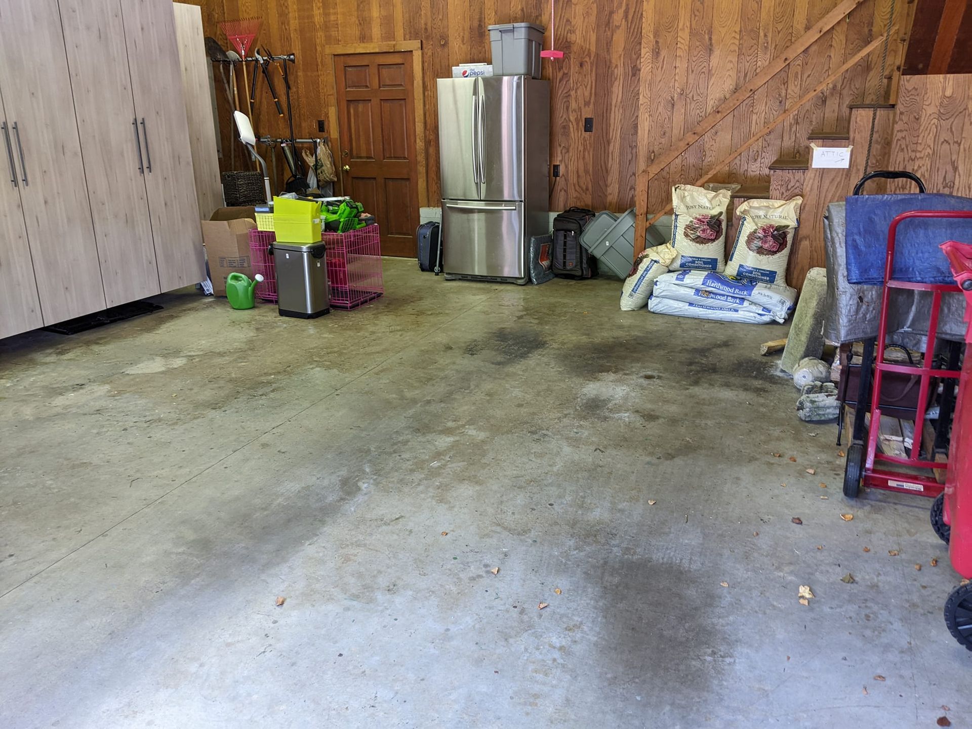 A storage area with concrete floors, a stainless steel refrigerator, storage cabinets, and bags of material on the right.