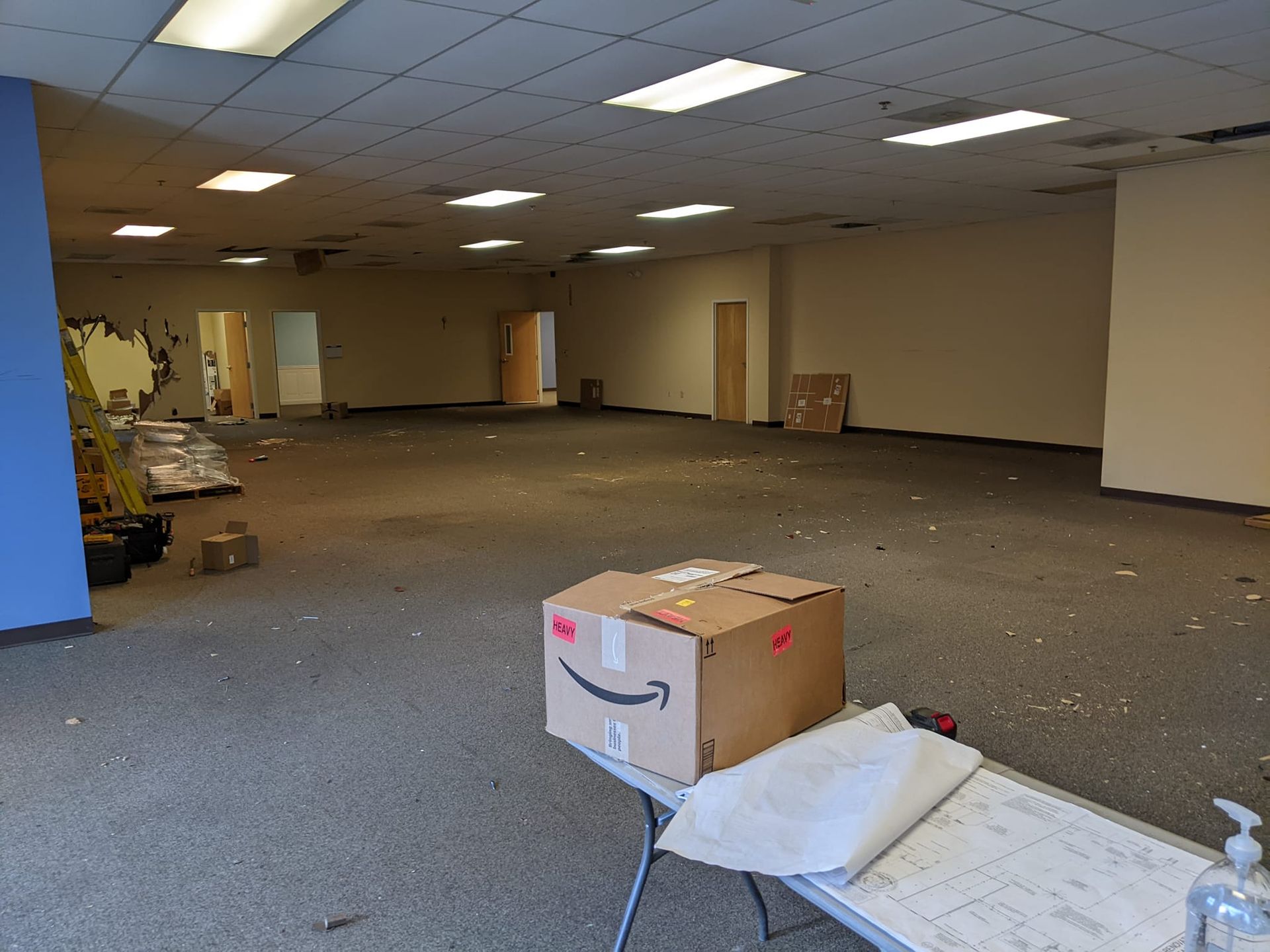 A large, empty office space with gray carpeting, drop ceilings, and an Amazon box on a table in the foreground.