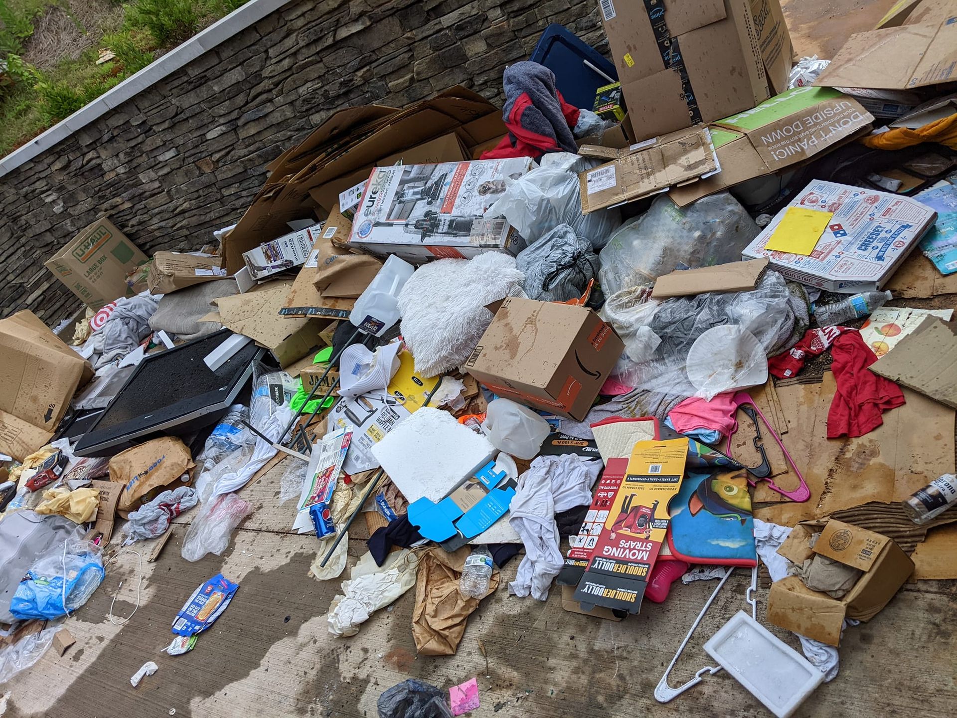 A pile of discarded trash, cardboard boxes, and miscellaneous debris scattered across a concrete ground.