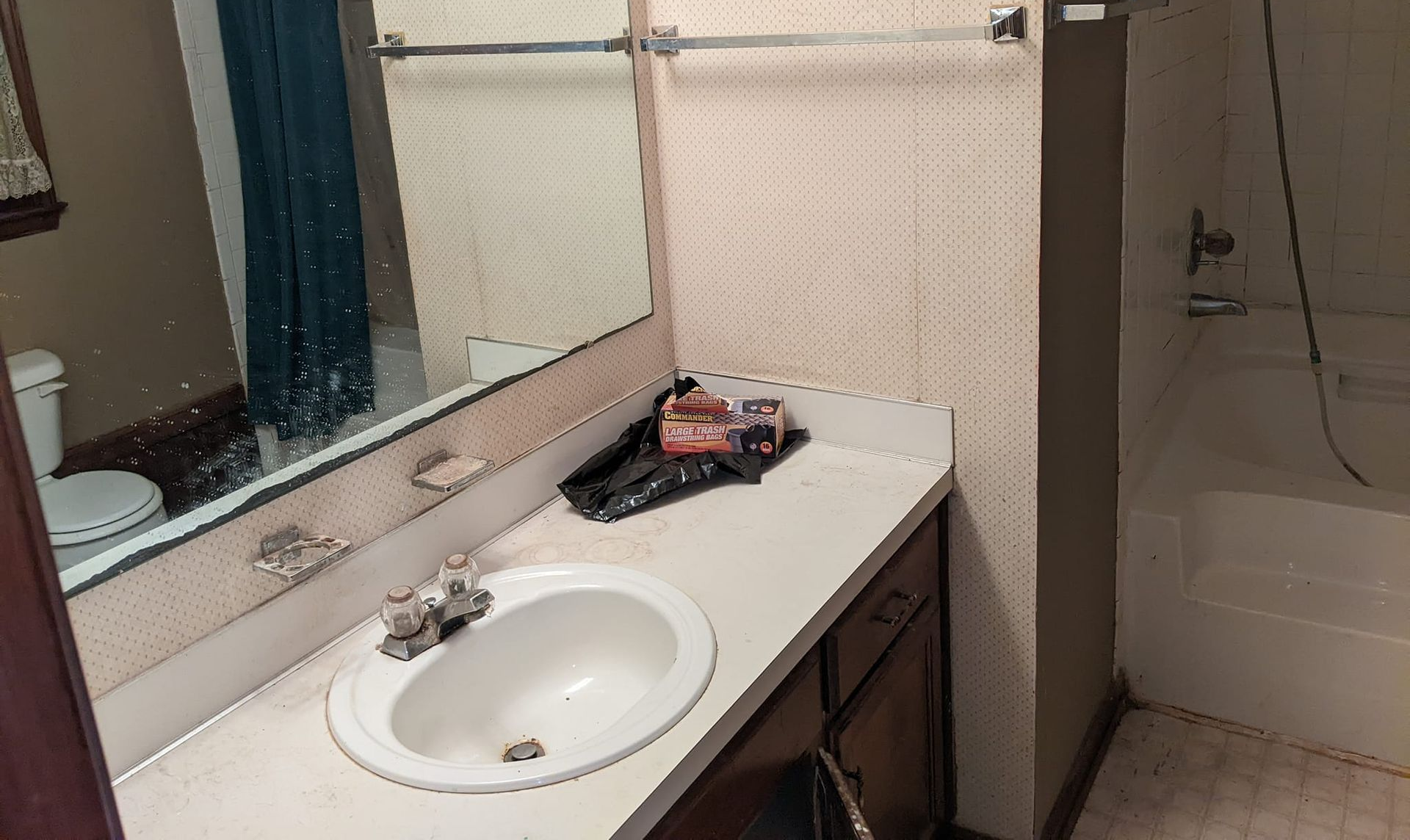 A bathroom vanity with a white sink, a mirror, and a small countertop, next to a toilet and a bathtub with a shower head.