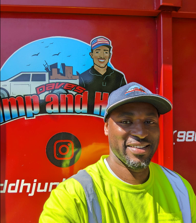 Man in neon safety shirt and cap smiling in front of a bright red sign with a cartoon logo.