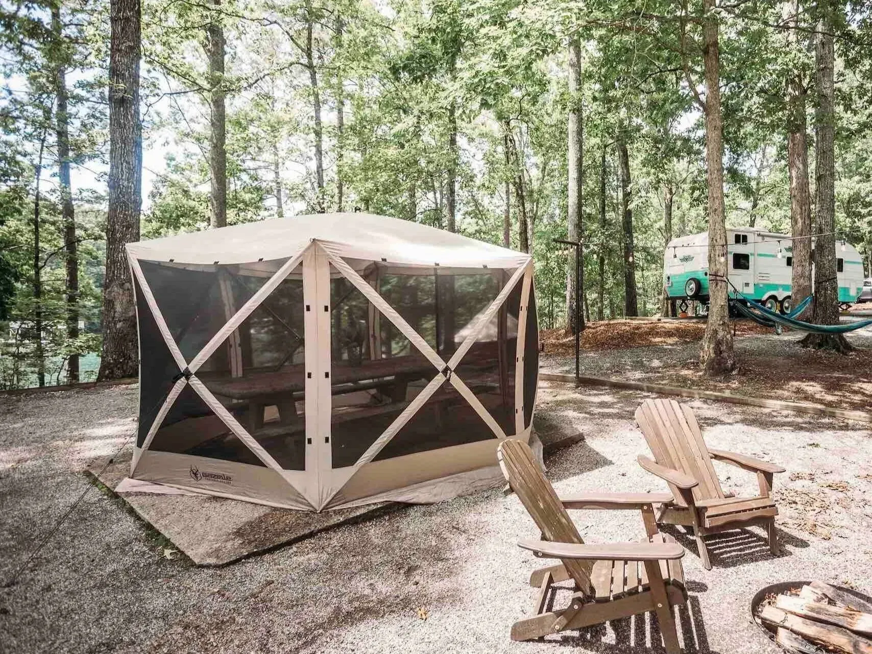 Screened gazebo with table, two chairs, and camper in a wooded campsite.