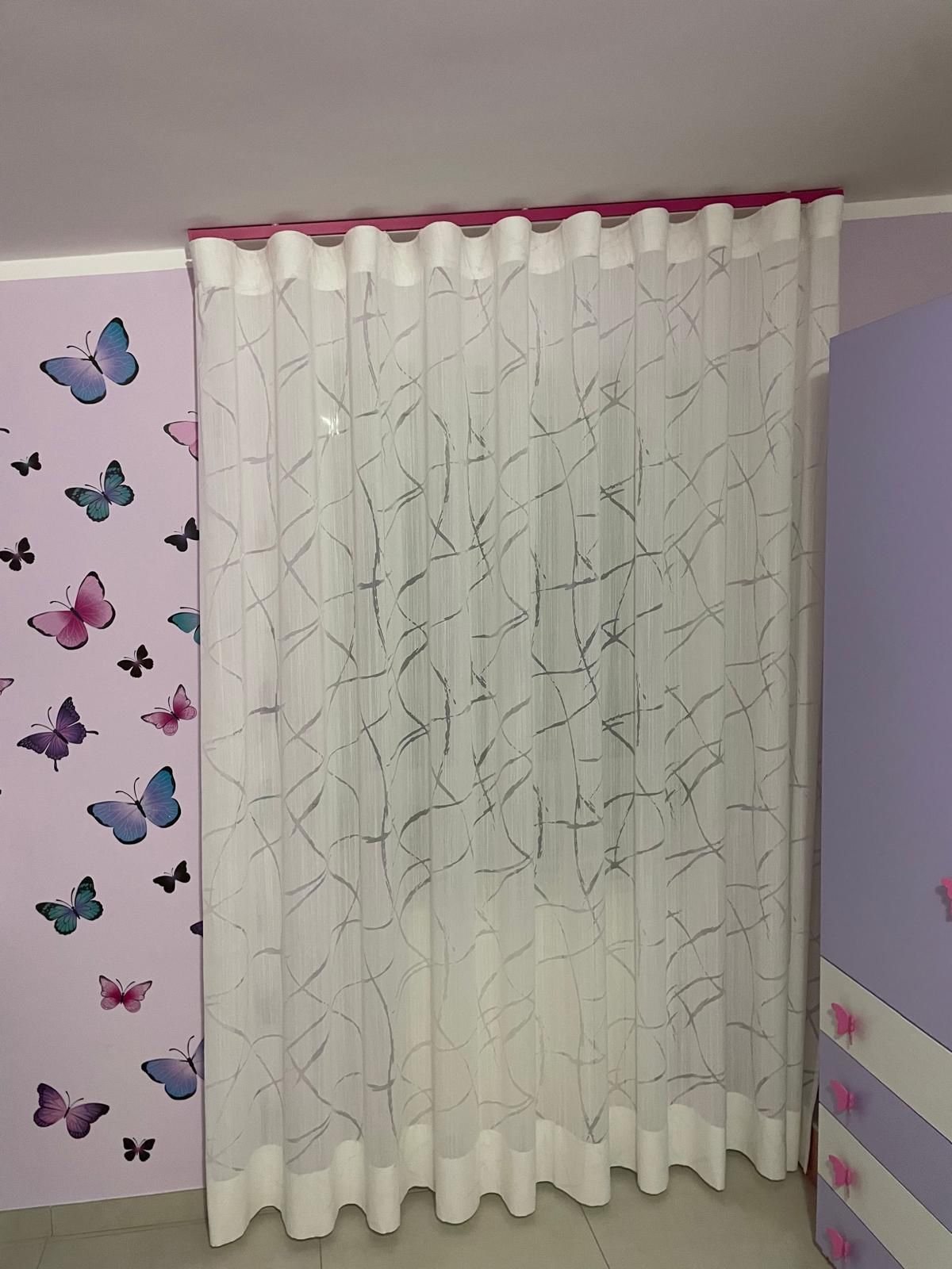 Tenda bianca trasparente con linee scure, appesa nella cameretta di un bambino con adesivi murali a forma di farfalla.