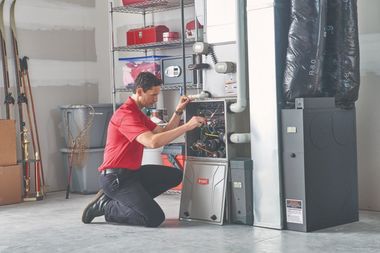 A man in a red shirt is working on an air conditioner in a garage.