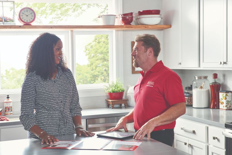 A man and a woman are standing in a kitchen talking to each other.