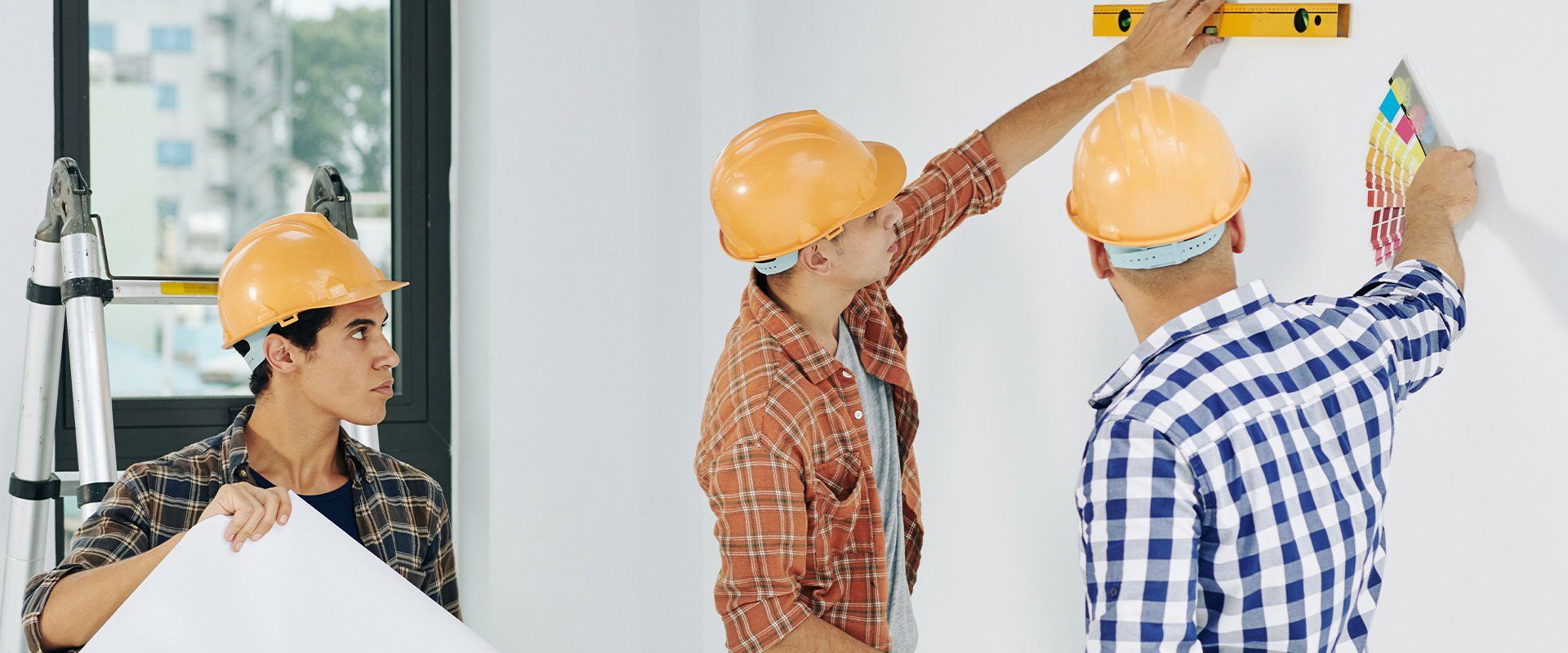 Two construction workers are measuring a wall with a level.