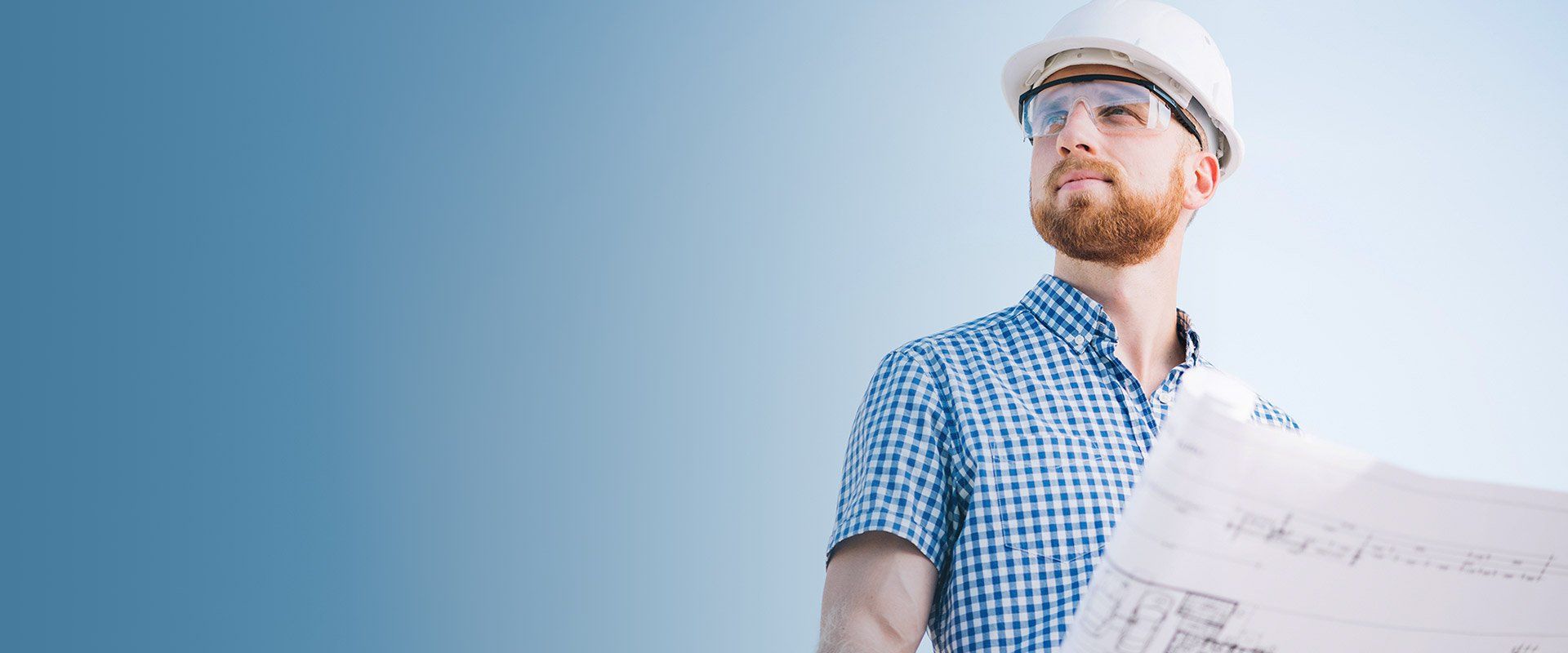 A man wearing a hard hat and goggles is holding a blueprint.