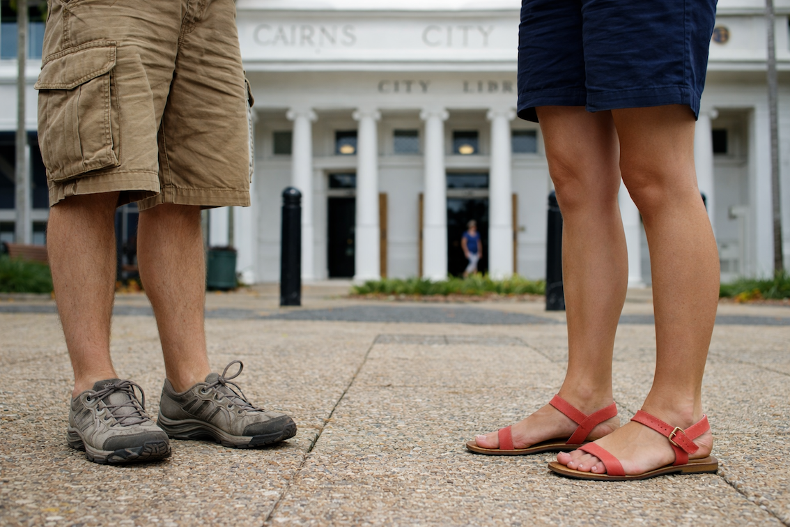 Two people standing side by side, shown only from the legs down, on a footpath outside the Cairns City Library and Cairns City Council building in tropical North Queensland, captured during a Cairns Urban Walking Tour in the CBD.
