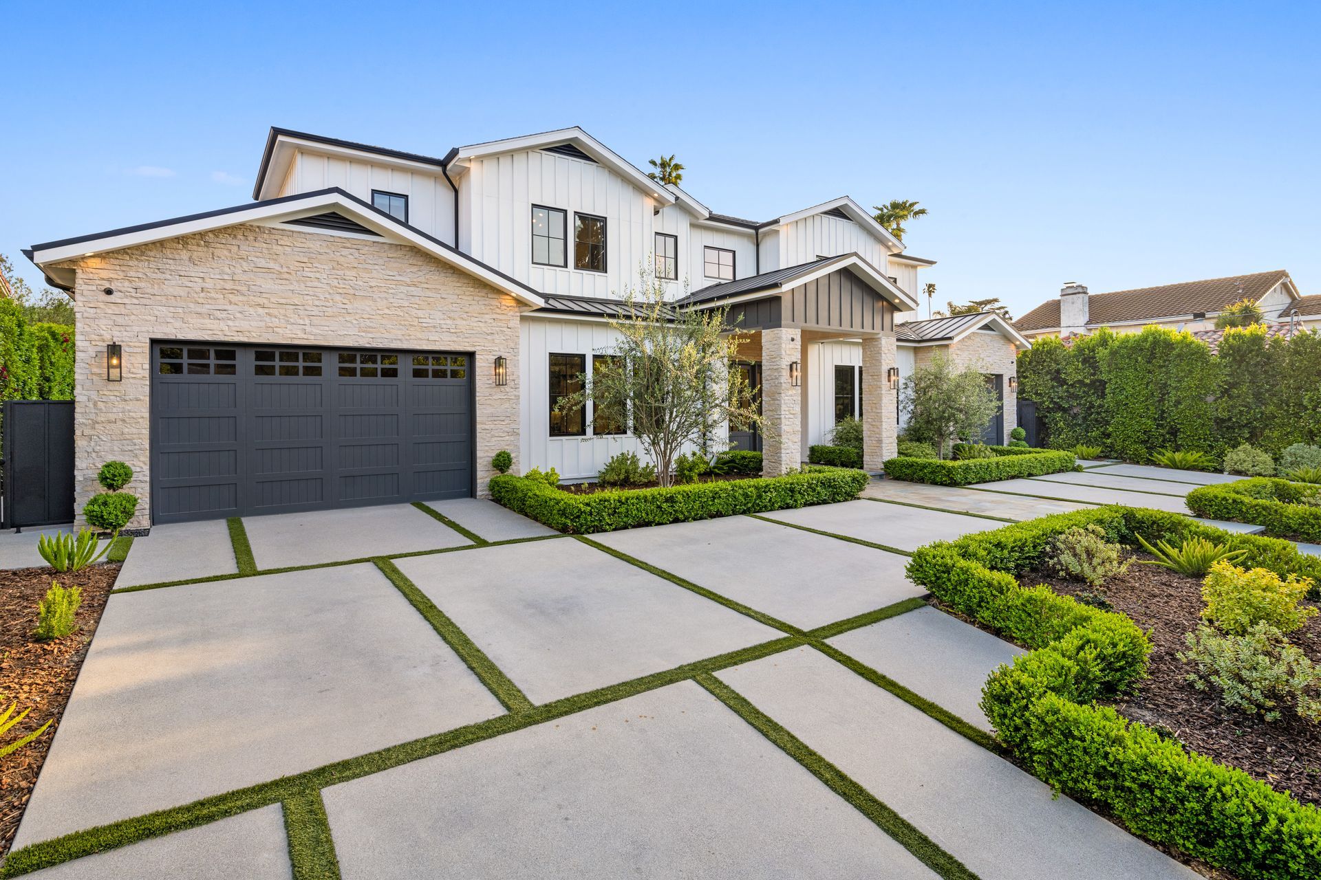 Modern two-story house with gray garage, stone facade, and landscaped front yard with driveway