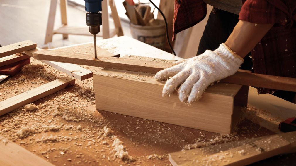 Person cutting wood with a power tool on a workbench, sawdust scattered around
