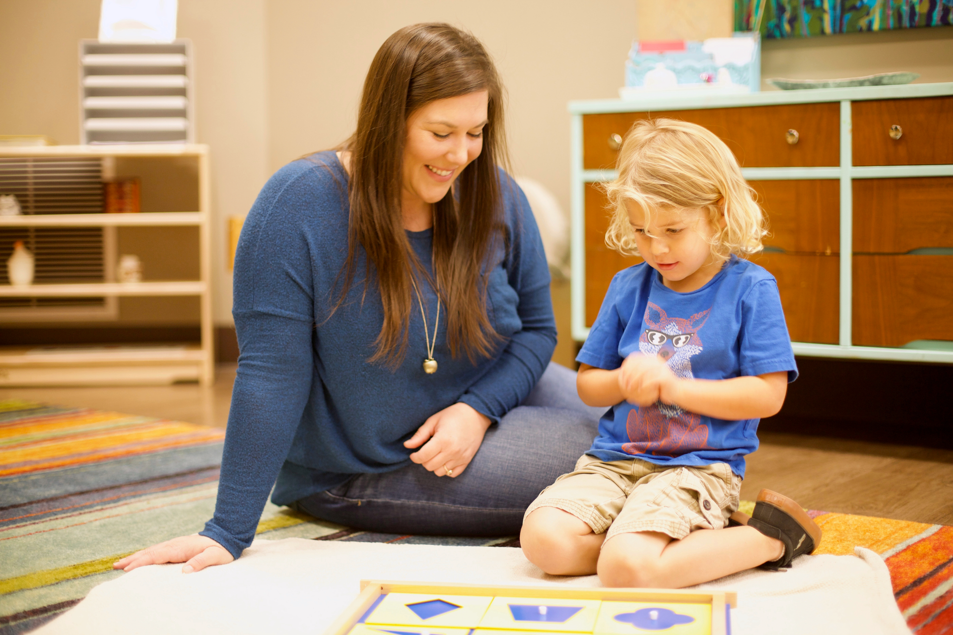 A Montessori guide is observing a child put together a wooden puzzle.