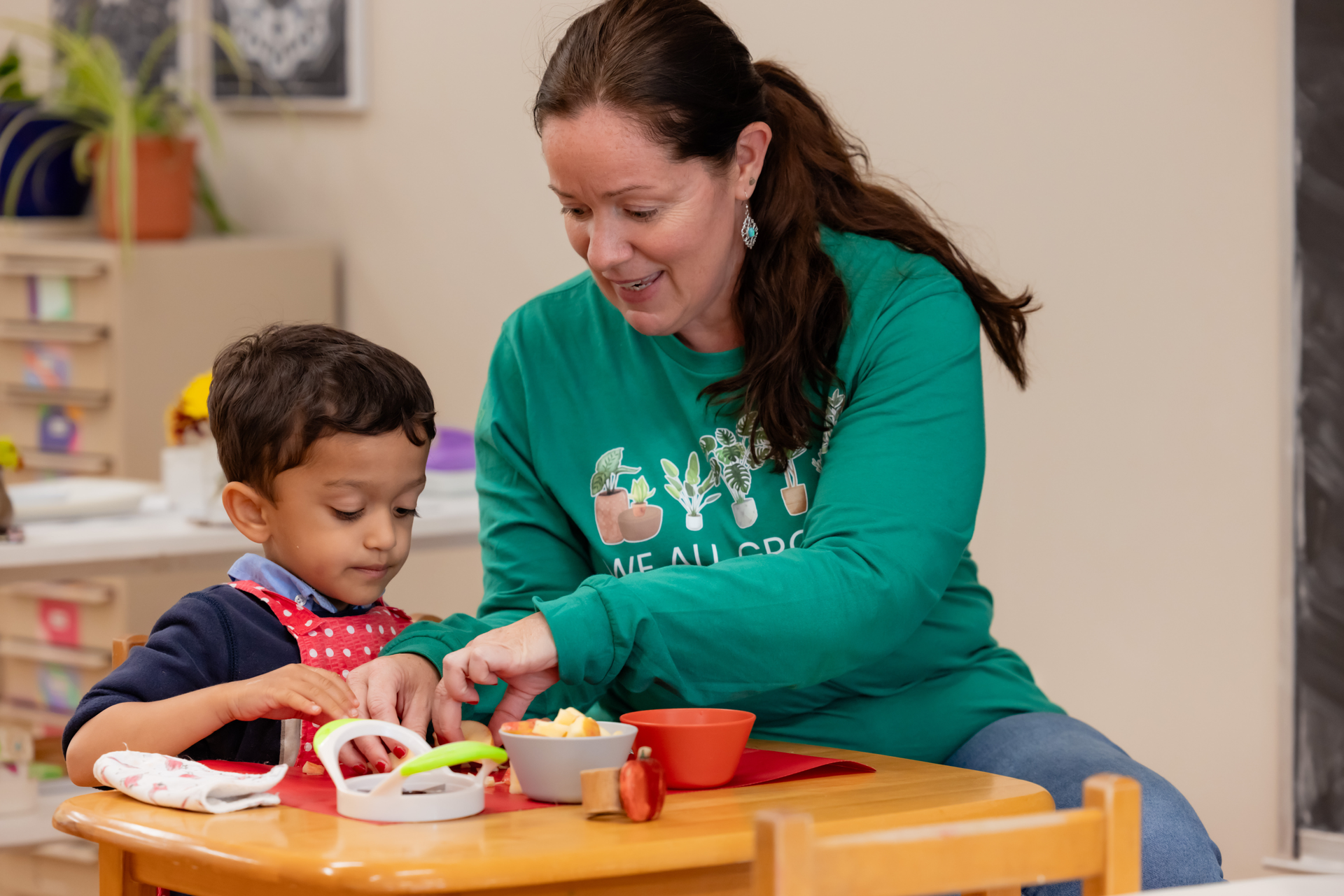 A Montessori teacher is helping a child cut fruit.