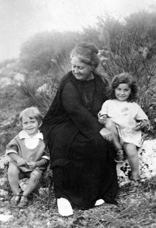 Dr. Maria is sitting on a rock with two children.