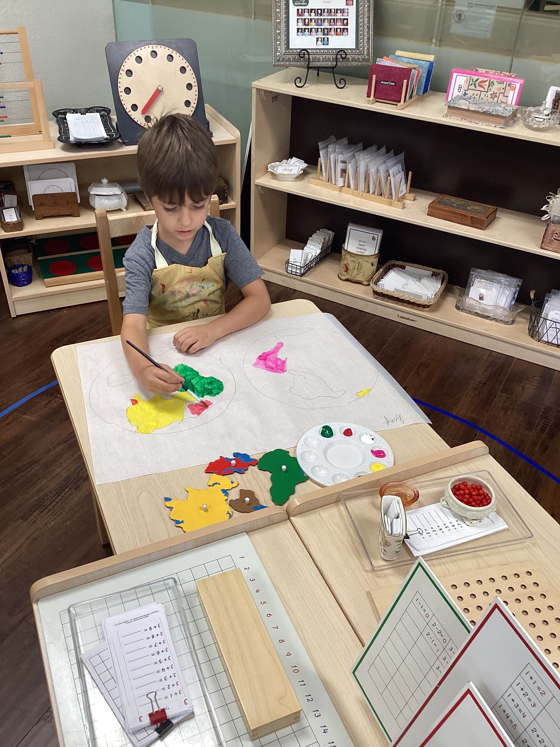 Montessori child sitting at a wooden table, painting a world map in the classroom.