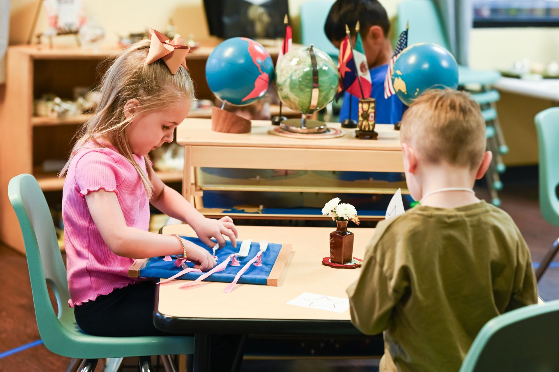 A Montessori student is sitting at a table working with a lacing frame.