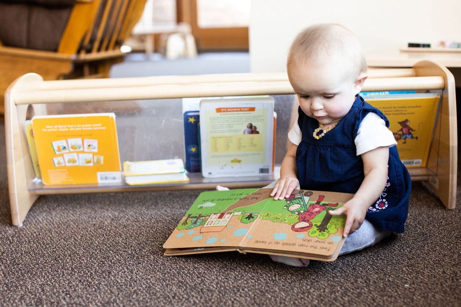 A Montessori infant is sitting on the floor and looking at a book.