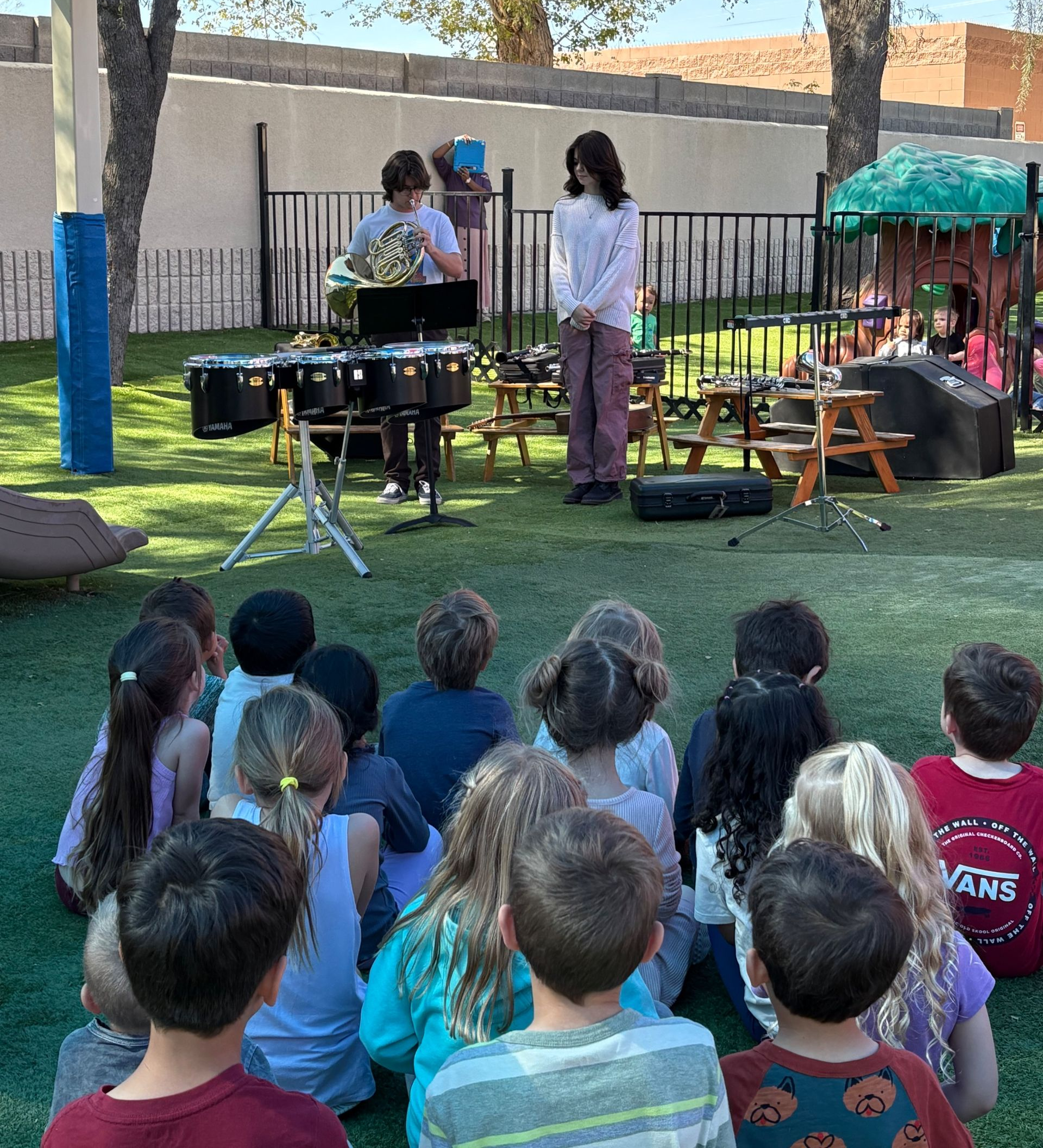 Montessori students watching a musical performance outdoors.