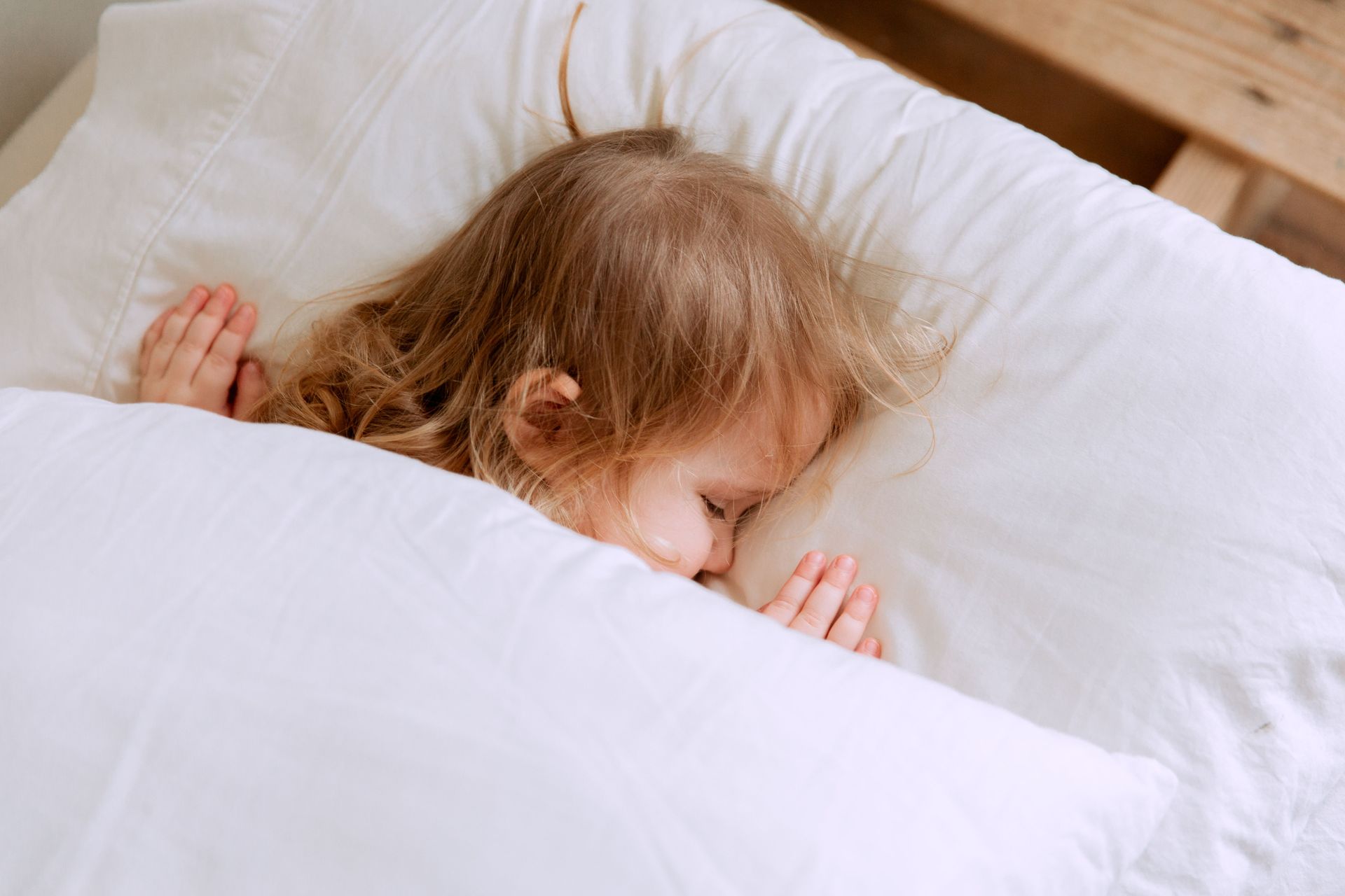 Sleeping child under a white blanket with a teddy bear nearby