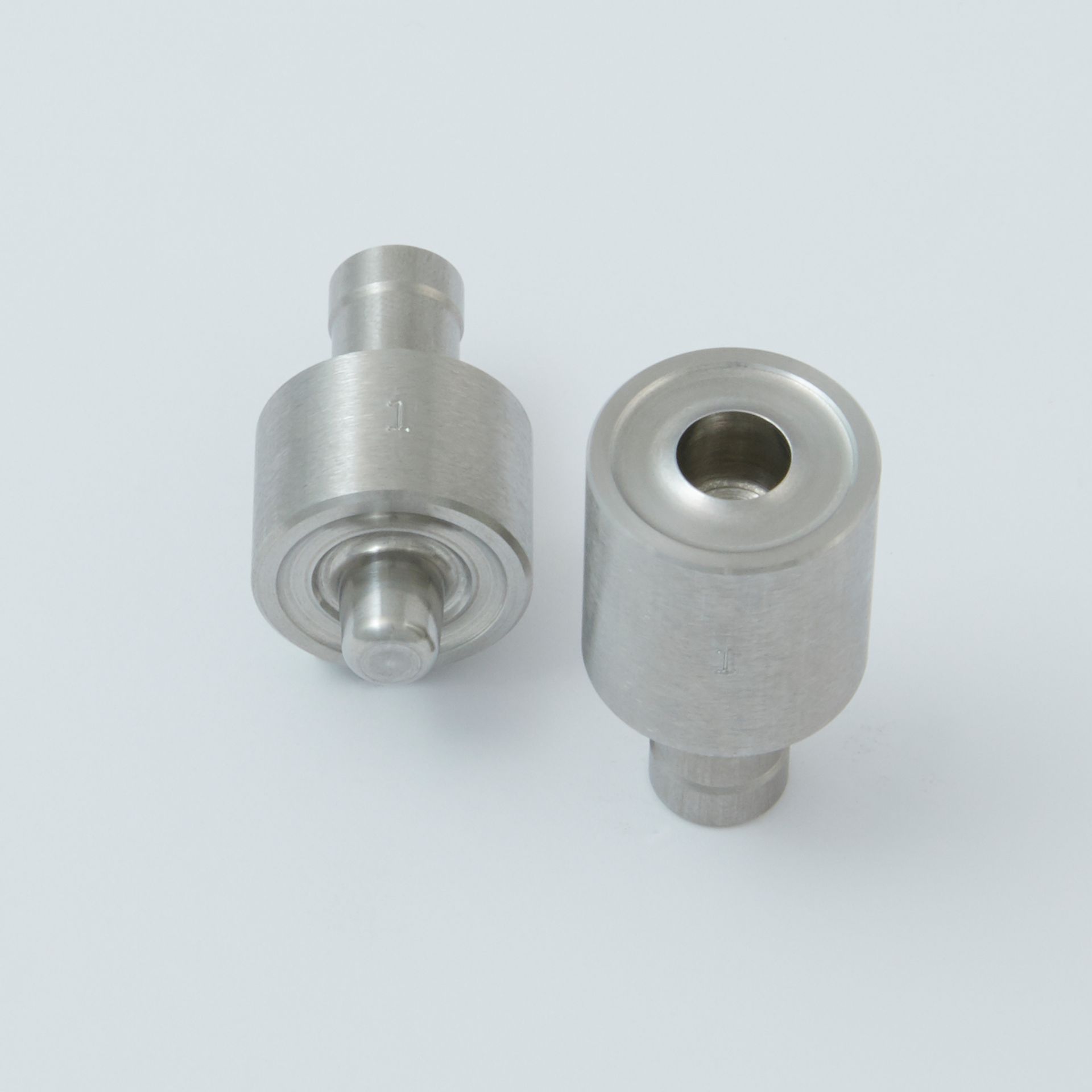 Two silver metal cylindrical parts with threaded ends on a light gray background