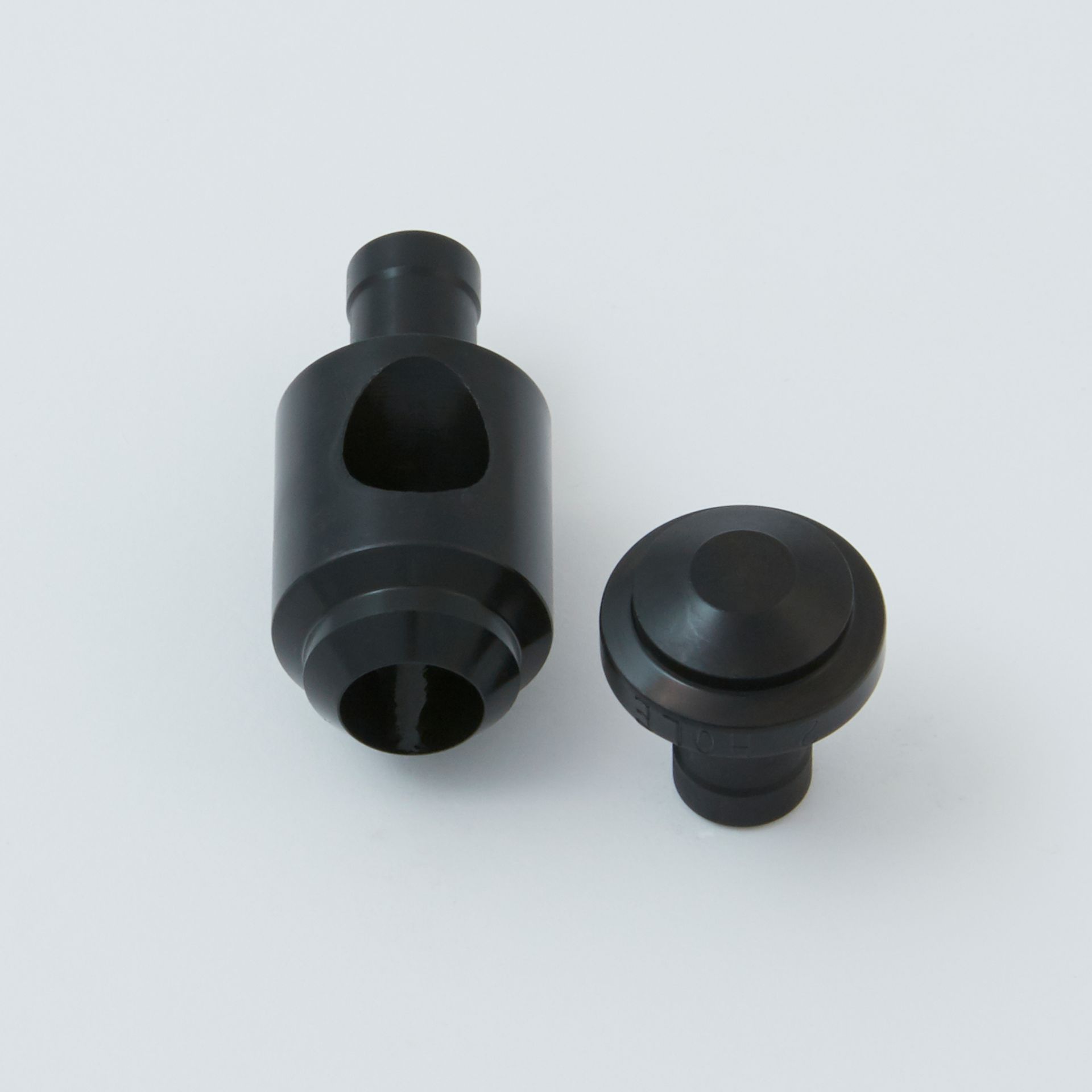 Two black, cylindrical plastic cord lock components, one assembled and one separated, shown against a white background.