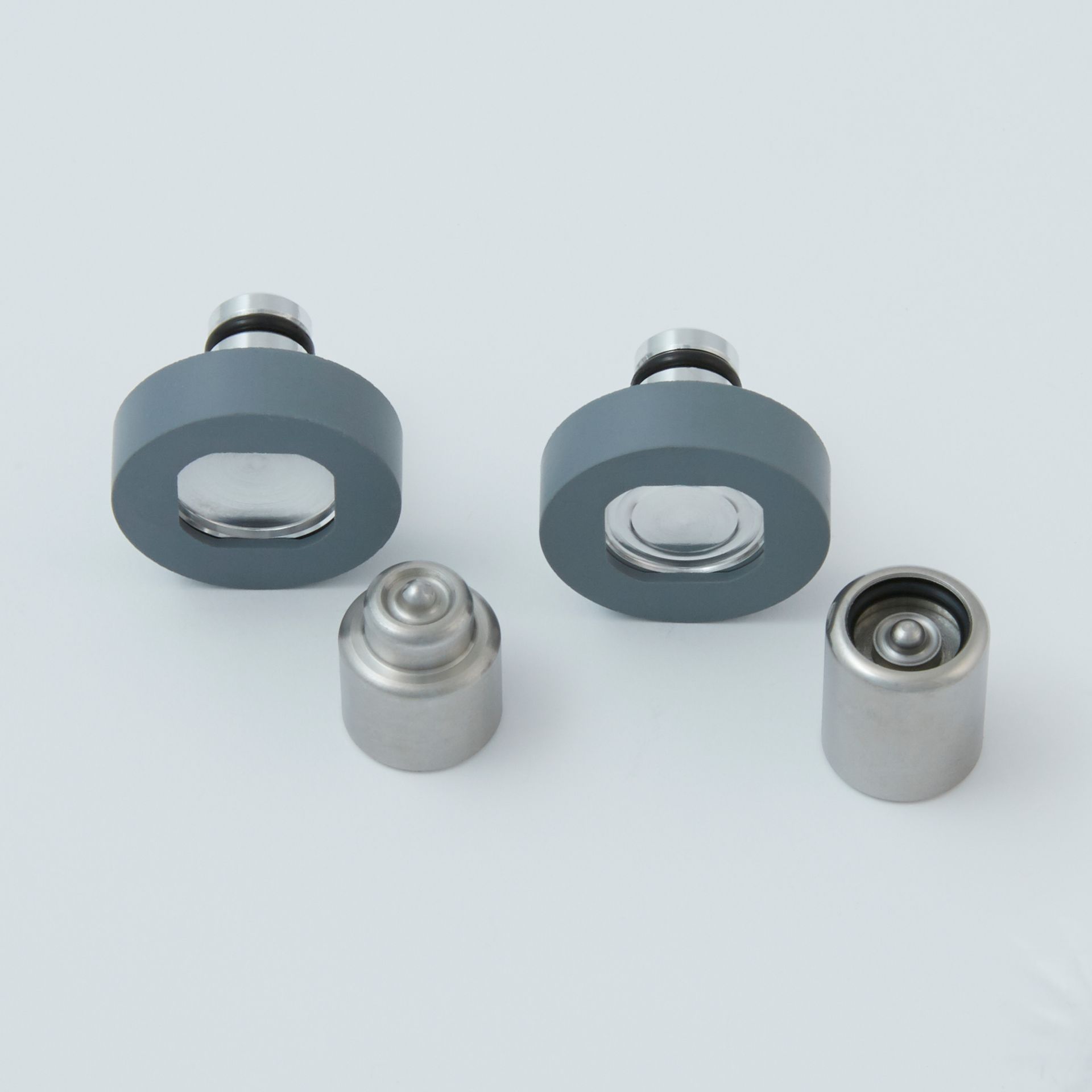 Two gray round metal components and two small silver cylindrical parts on a light background
